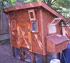 a chicken coop built into the side of a fenced in area with a trash can next to it