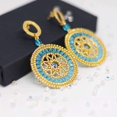 a pair of blue and gold earrings sitting on top of a black box next to some crystals