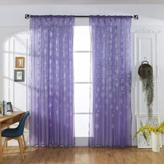 a purple curtain hanging in front of a window next to a wooden table and chair