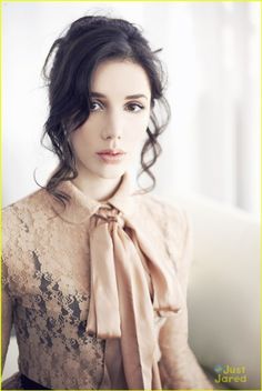 a young woman wearing a brown shirt and a beige scarf around her neck is looking at the camera