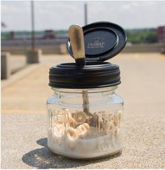 a glass jar filled with lots of sand and sea shells sitting on top of a sandy beach