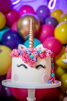 there is a cake with a unicorn face on it and balloons in the back ground