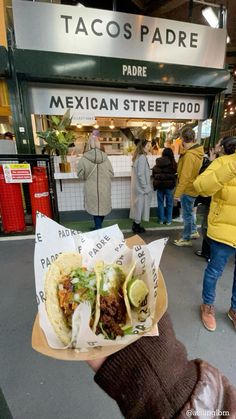 a person holding up a taco in front of a store