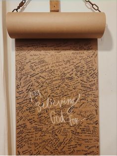 a cork board with writing on it hanging from a chain in front of a white wall