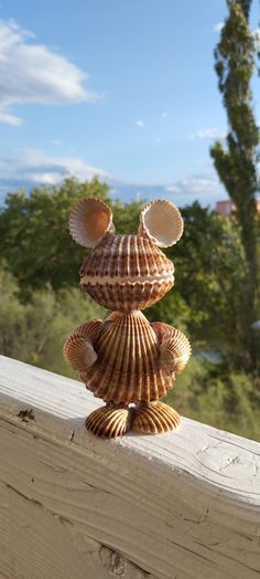 a sea shell figurine sitting on top of a wooden ledge next to trees