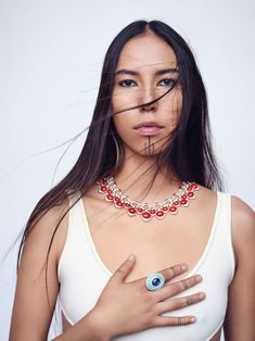 a woman wearing a necklace with an evil looking eye on it's chest and holding her hands in front of her face