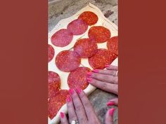 the woman is making a pizza with pepperoni slices on it and her nails are pink