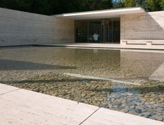 an empty pool in front of a building with rocks on the ground and water running through it