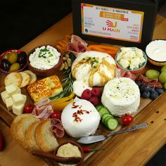 an assortment of cheeses, meats and fruit on a wooden platter with a sign in the background