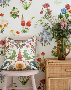 a pink chair next to a vase with flowers on it and a wall paper behind it