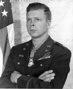 black and white photo of a man in uniform with arms crossed next to an american flag