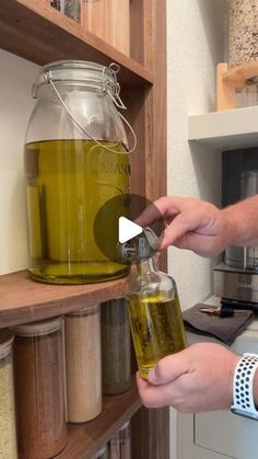 a person is pouring liquid into a glass jar on a shelf in a kitchen with wooden shelves