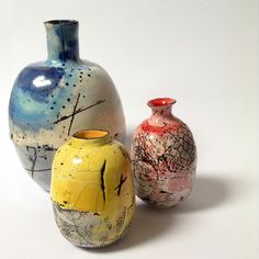 three colorful vases sitting next to each other on a white surface with no one around them