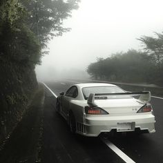 a white sports car driving down a road in the fog