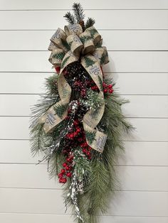 a christmas wreath hanging on the side of a white building with evergreen and berries around it