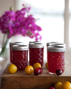 three jars filled with fruit sitting on top of a wooden table next to purple flowers