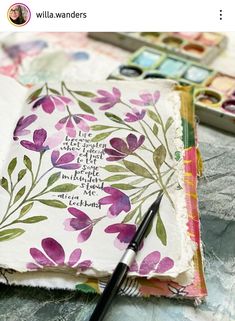 an open book with flowers on it and a pen resting on the cover next to it