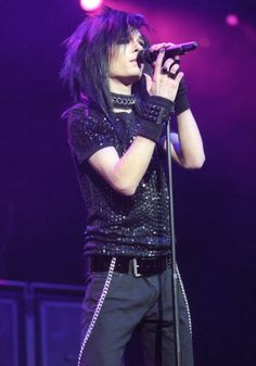 a man with black hair holding a microphone in front of his face while standing on stage