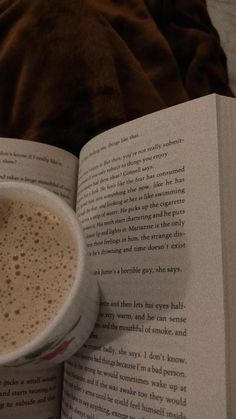 a cup of coffee sitting on top of an open book next to a brown blanket