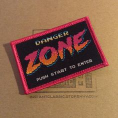 a pink and black patch with the words danger zone on it, in front of a cardboard box