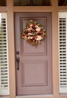 a wreath on the front door of a house with shutters and flowers in it