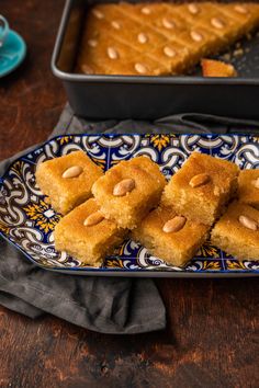 several pieces of cake on a blue and white plate next to a pan with almonds