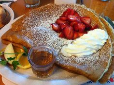 a white plate topped with pancakes covered in powdered sugar and strawberries next to fruit