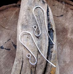 a pair of silver earwires sitting on top of a piece of driftwood