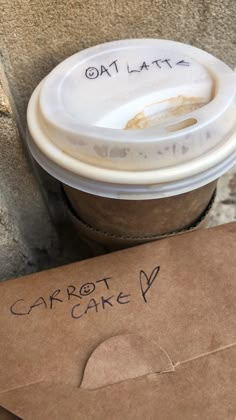 a brown paper bag with writing on it next to a coffee cup that says carrot cake