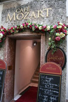 the entrance to cafe mozzart is decorated with flowers and chalkboard menus