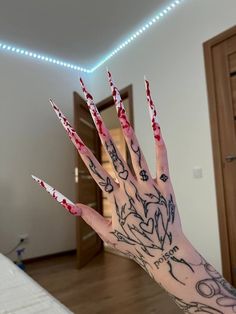 a person's hand with red and black nail polish on it in front of a bed