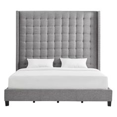 an upholstered bed with two pillows and white linens on the headboard