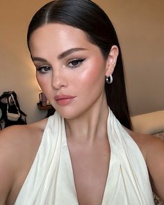 a woman with long dark hair wearing a white halter top and silver hoop earrings