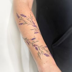 a woman's arm with purple flowers and leaves tattooed on her left arm, in front of a white background