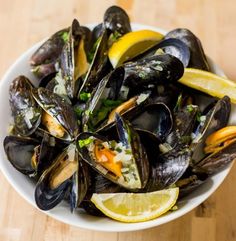 a white bowl filled with mussels and lemon wedges