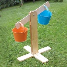 two buckets are hanging from a wooden stand in the grass, one is blue and orange