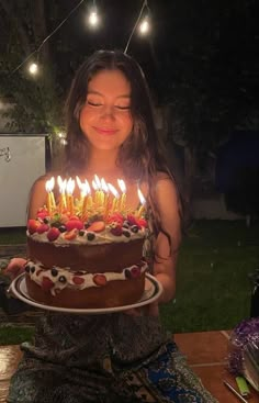 a woman holding a cake with lit candles on it in front of her face and eyes