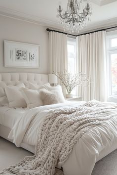 a white bedroom with a chandelier, bed and window in the corner that has curtains on both sides