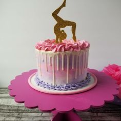 a pink and gold birthday cake with a figure on top that has icing dripping from it