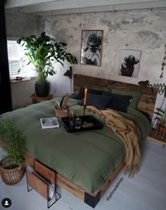 a bed with green sheets and pillows in a room next to potted plants on the floor