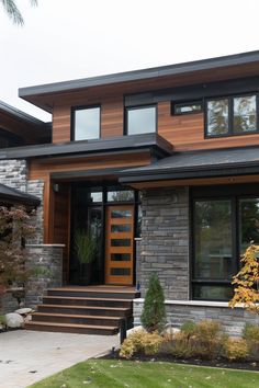 a modern house with stone and wood sidings on the front door, steps leading up to it