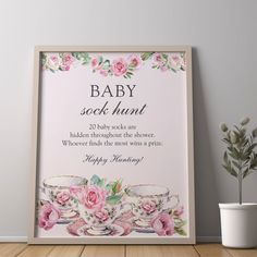 a baby shower sign with pink roses and teacups on the table next to a potted plant