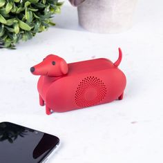 a red dog shaped speaker sitting on top of a table next to a cell phone