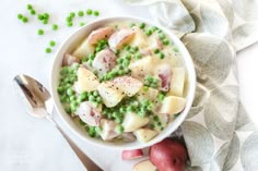 a white bowl filled with peas and potatoes next to two spoons on top of a table