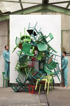 two men standing next to a large stack of green and yellow chairs in front of a white wall