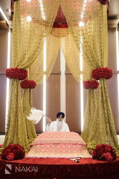 a man sitting on top of a bed in front of a red and gold canopy