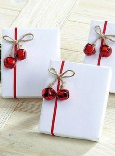 two white gift boxes tied with red ribbon and bell ornaments are sitting on a wooden table