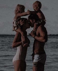 three people standing on the beach and one is holding a baby