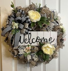 a welcome wreath with flowers and ribbon hanging on a door handle that says welcome in black and white