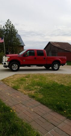 a red pick up truck is parked in front of a barn with an american flag on it